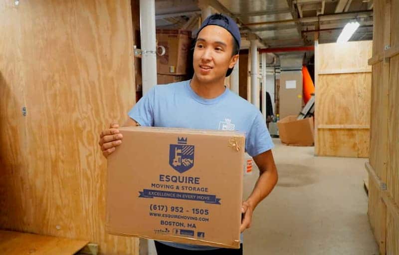 Esquire storage employee carrying a labeled moving box