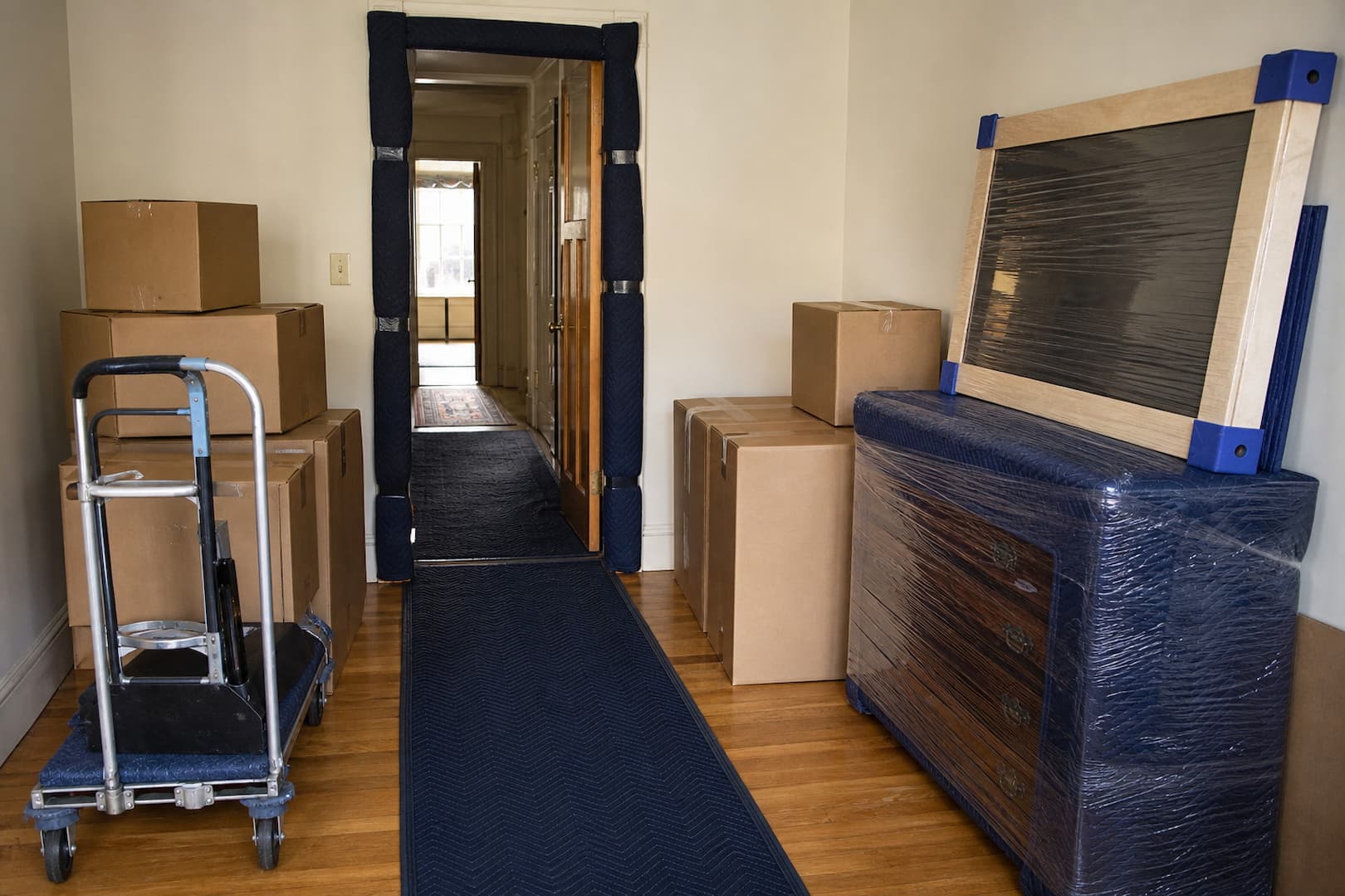 Furniture, artwork, cartons, doorway padding, floor runner, and moving dolly prepared for loading