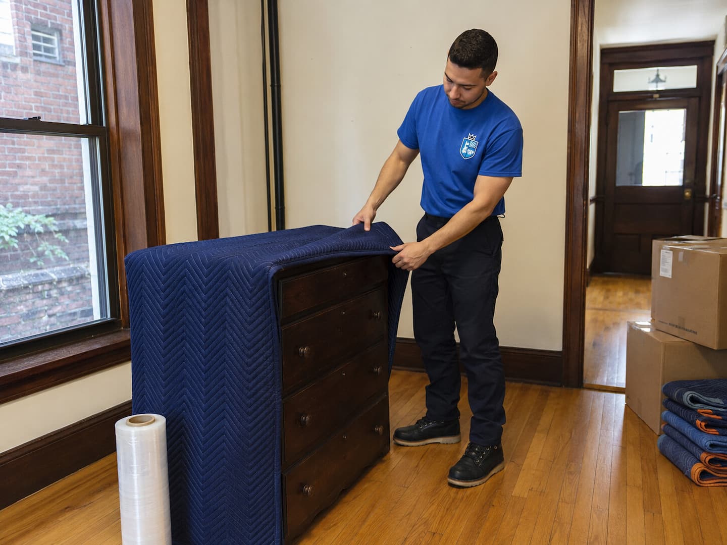 Esquire movers wrapping a wooden dresser in a Boston home for interstate transportation