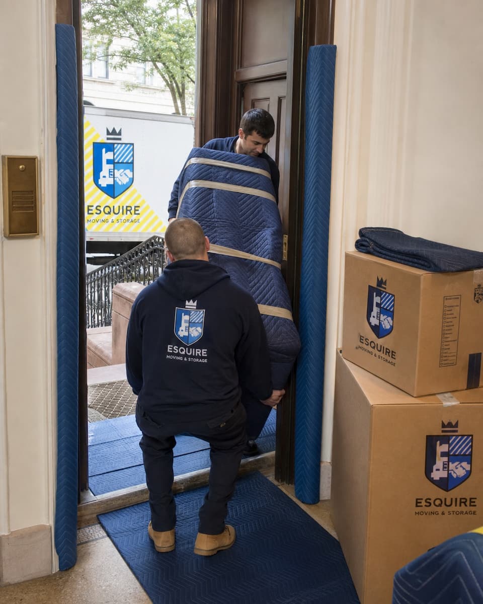 Esquire movers guiding a protected dresser through a New York brownstone doorway