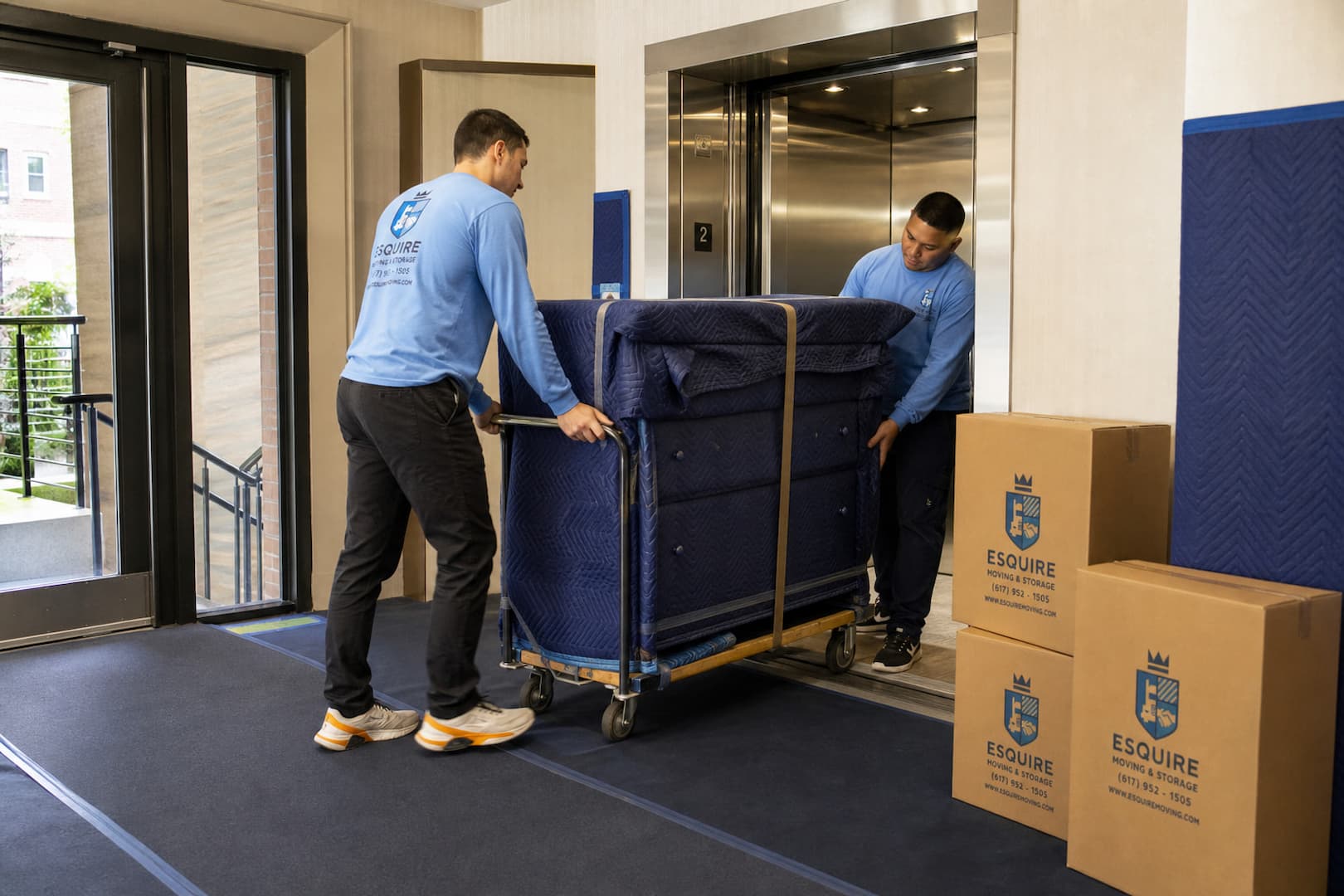 Esquire movers guiding blanket-wrapped furniture from a New York apartment freight elevator